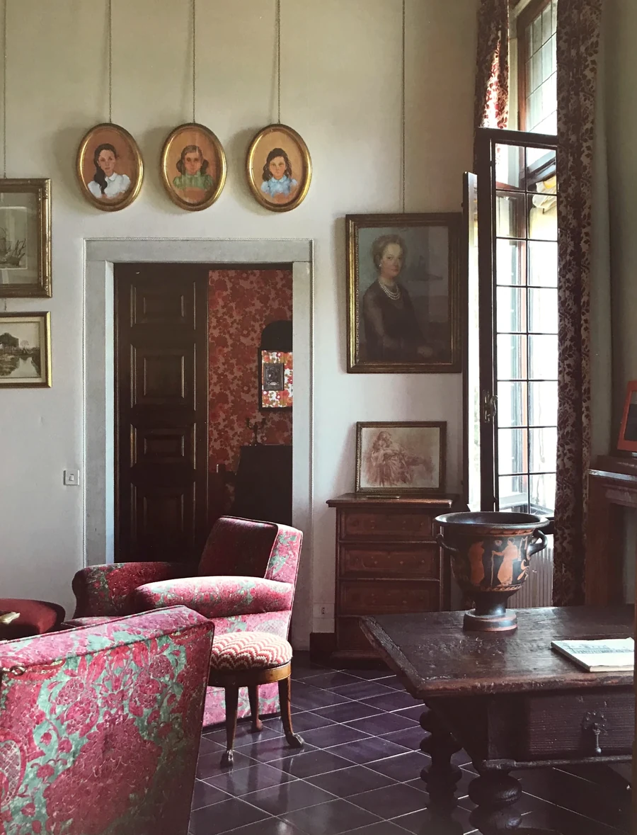 A drawing room where family portraits hang above a doorway, an open casement letting in afternoon light.