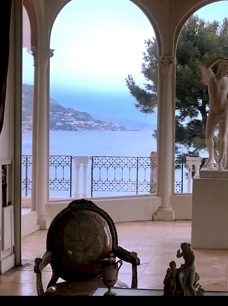 A marble figure on a plinth framed by the loggia arcade, the coast beyond.