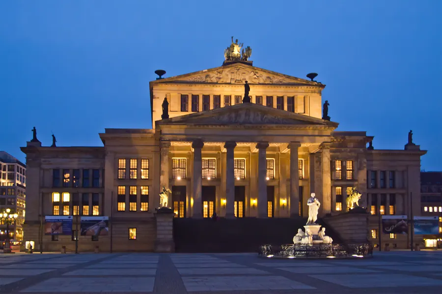 A neoclassical concert hall on a Berlin square at blue hour, its windows lit warmly.