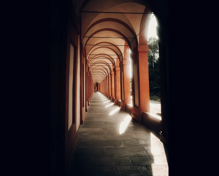 A long arcaded portico, daylight falling in bands across the stone floor.