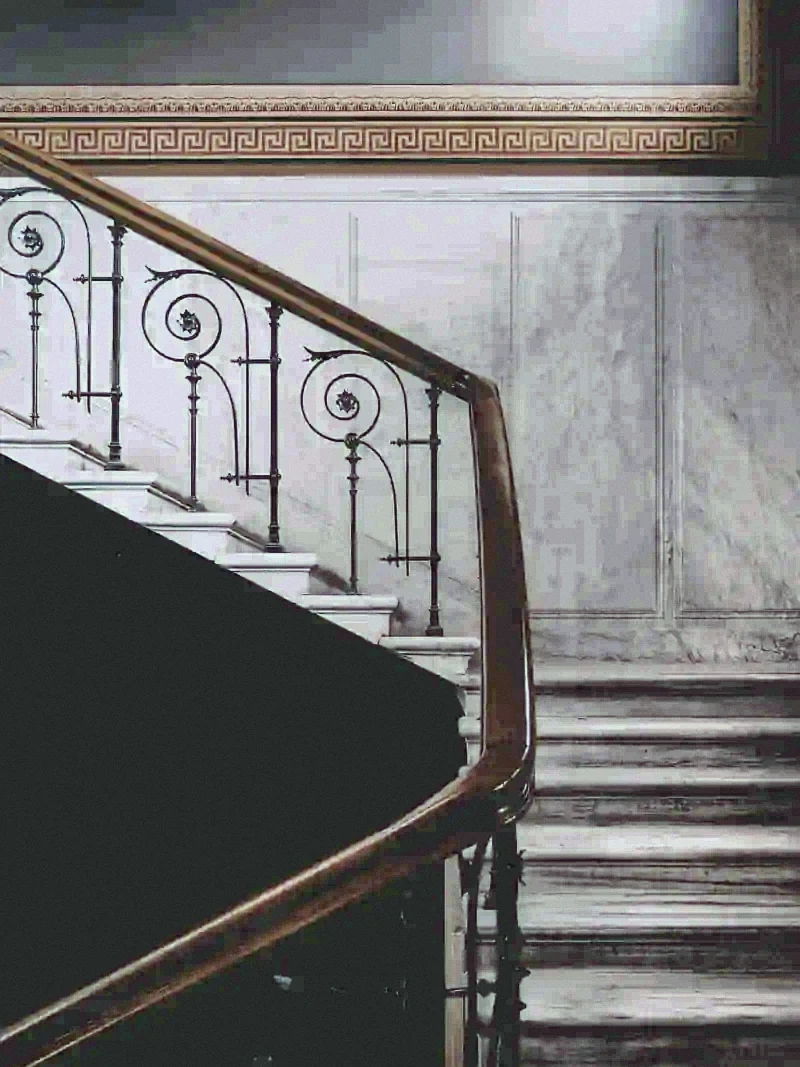 A marble stair with a polished brass handrail and iron balustrade in an old city house.