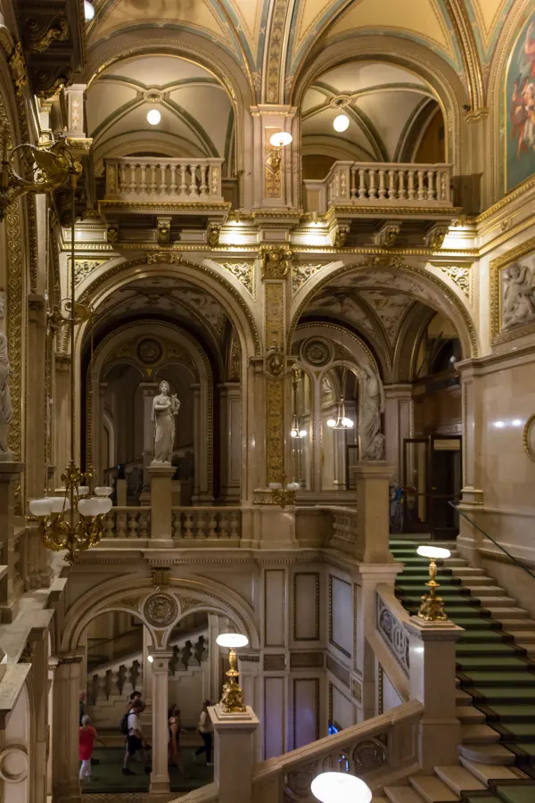 The grand staircase of the Vienna State Opera, lit warmly beneath painted vaults.
