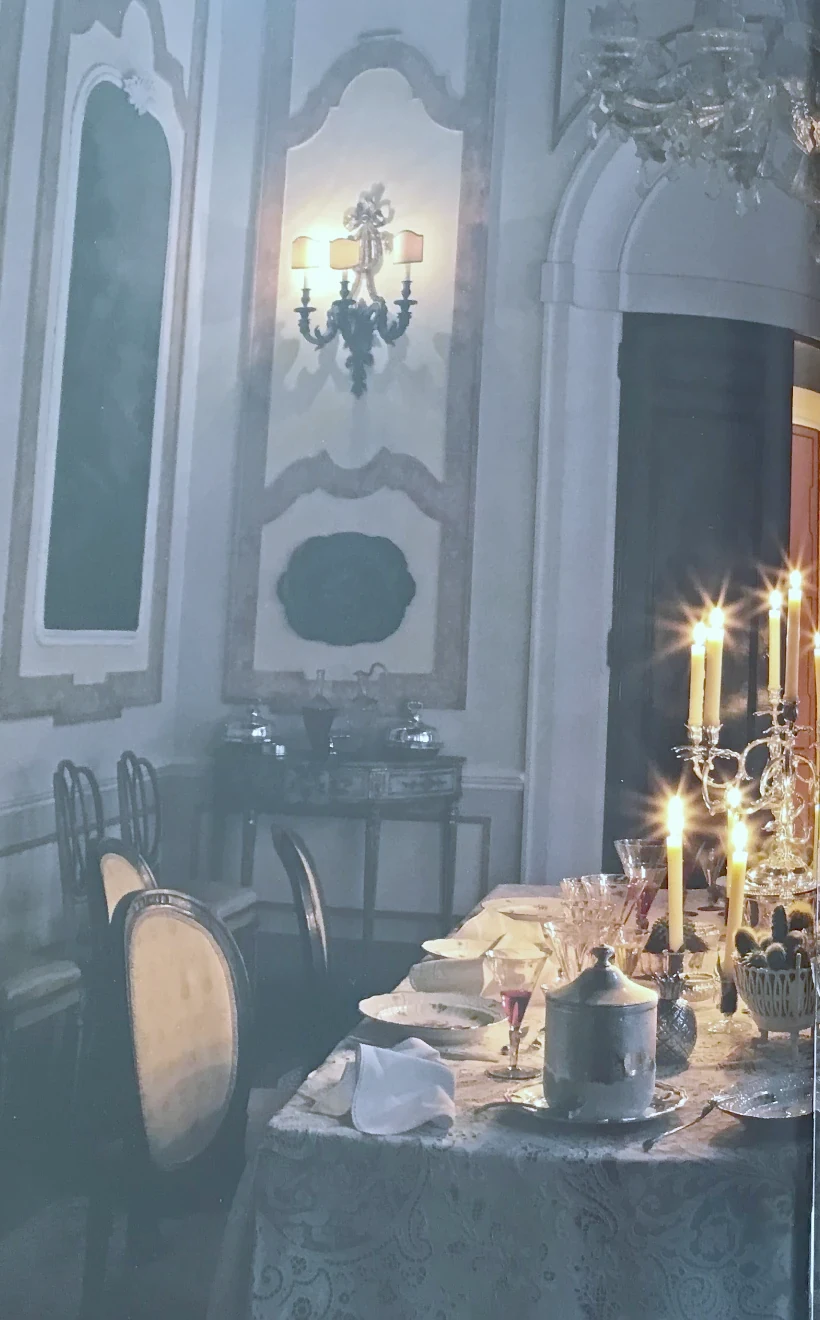 A dining room at night, candles lit along a long linen table beneath painted panelling.