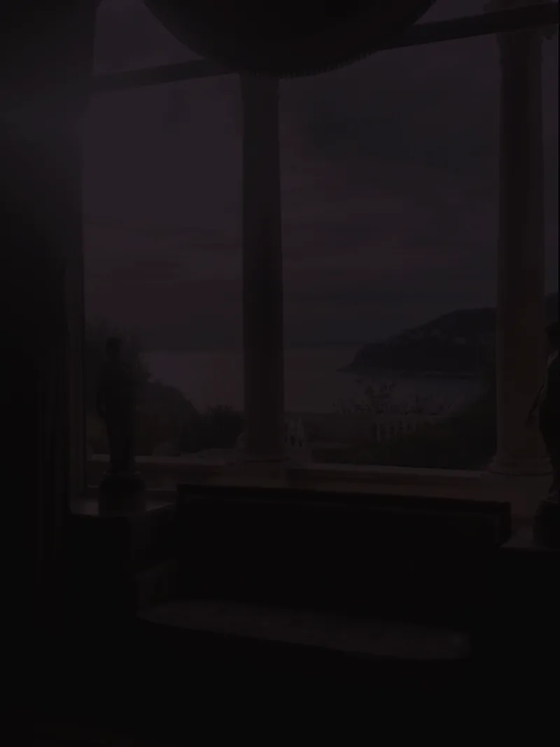 A window seat behind stone columns at dusk, overlooking calm water.